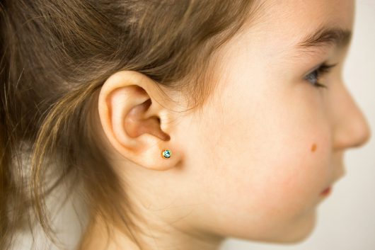 Ear piercing in a child - a girl shows an earring in her ear made of a medical alloy